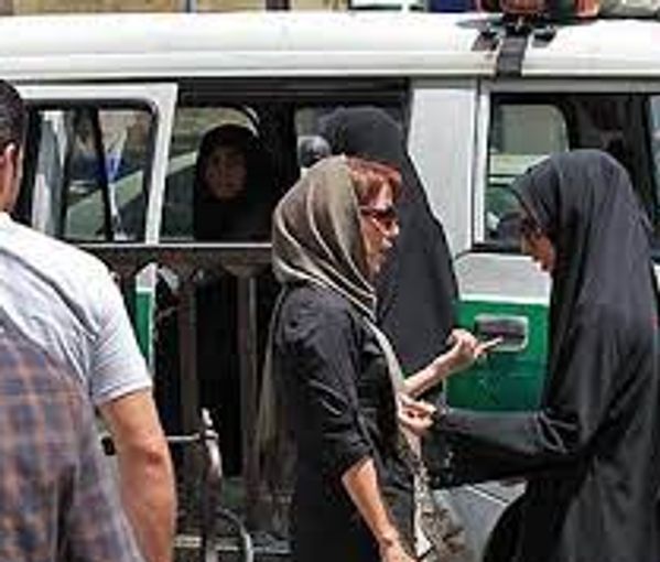 A hijab police patrol with black-cladded agents stopping women in the street to demand a full headscarf. Undated