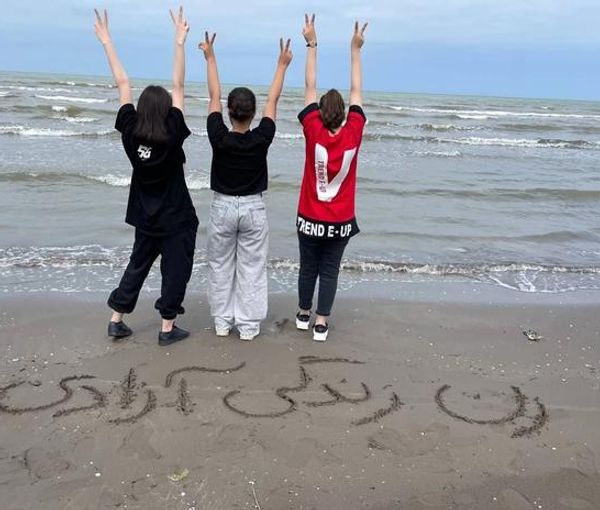 Young women with the slogan "Woman, Life, Freedom" written on the sand. Undated