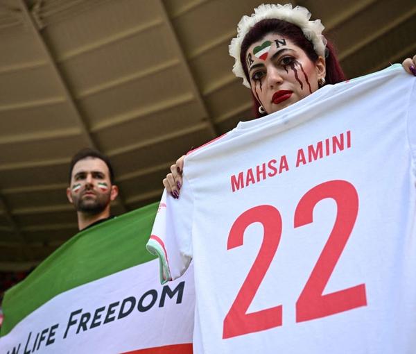 Two Iranian fans holding a jersey in memory of Mahsa Amini, whose death in custody sparked the ongoing protests, and a flag with the main motto of the protests before they were confronted by the Qatari police 