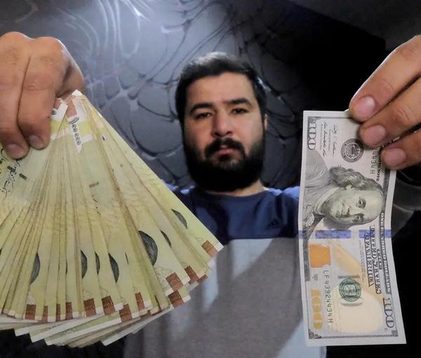 A money changer poses for the camera with a US hundred dollar bill (R) and the amount being given when converting it into Iranian rials (L), at a currency exchange shop in Tehran's business district, Iran, January 20, 2016. 