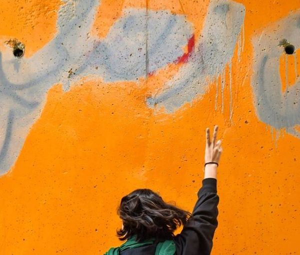 An Iranian woman standing in front of a wall on which the main slogan of the ongoing protests – Women, Life, Liberty – is seen despite the government’s attempts to cover it