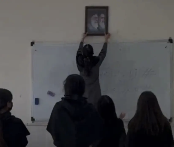 A schoolgirl pulling down a photo of Iran’s current and former rulers  (October 2022)
