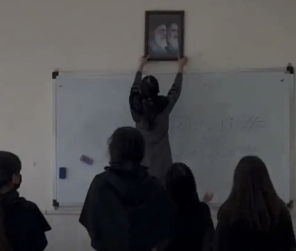 A schoolgirl pulling down a photo of Iran’s current and former rulers (October 2022)