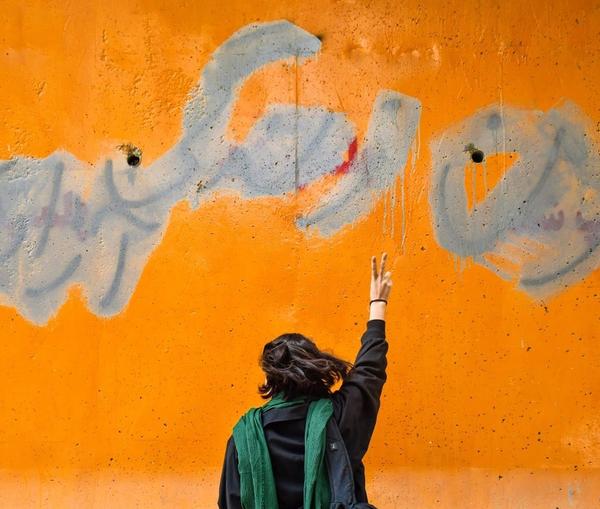 An Iranian woman standing in front of a wall on which the main slogan of the ongoing protests – Women, Life, Liberty – is seen despite the government’s attempts to cover it 