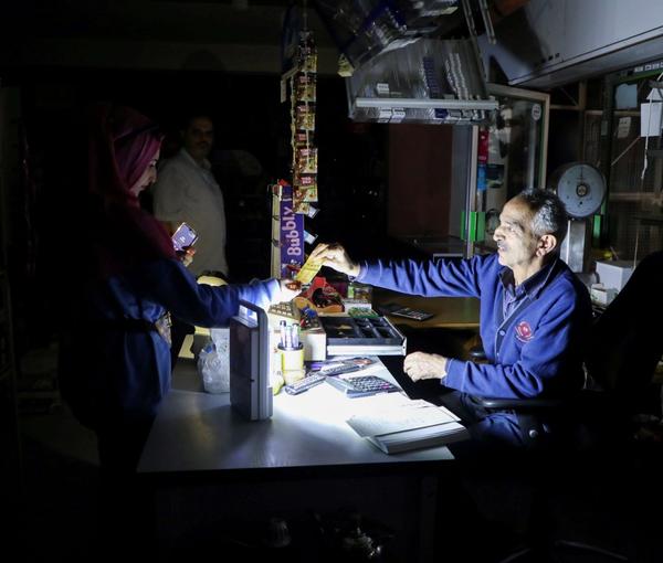 People shop in a grocery store under a portable electric light during a power cut near Bhamdoun, Lebanon, October 9, 2021.