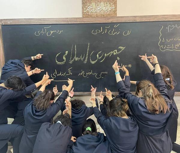Iranian schoolgirls showing finger to a blackboard with “the Islamic Republic” words written on it (file photo)